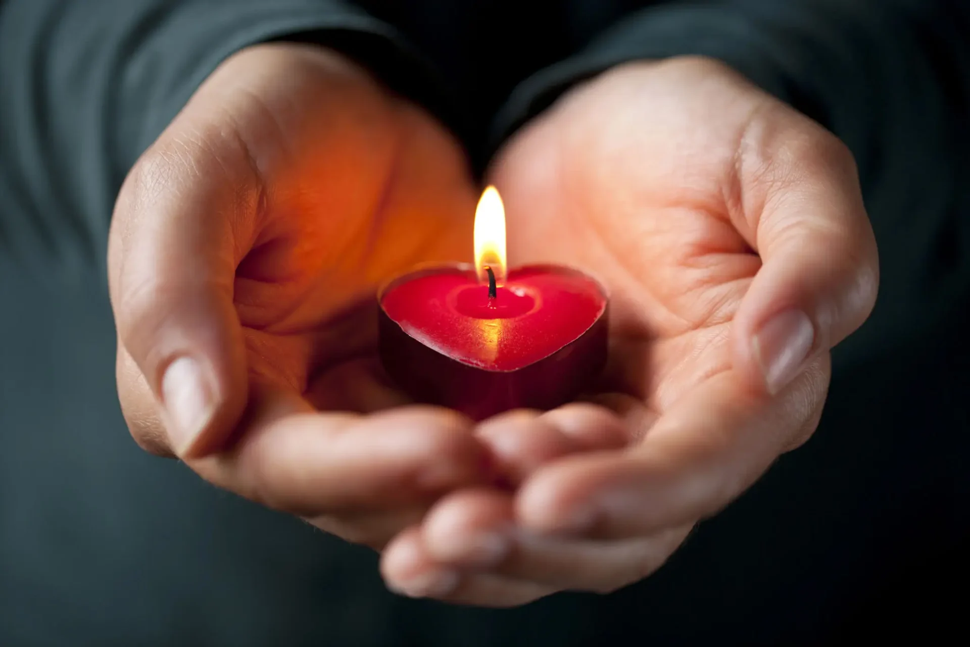 Hands gently holding a lit heart-shaped candle.