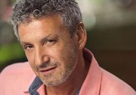 Portrait of a middle-aged man with curly gray hair and a pink shirt.