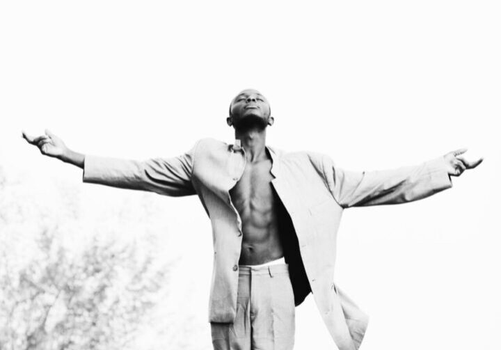 Man in coat standing with arms outstretched, looking up.